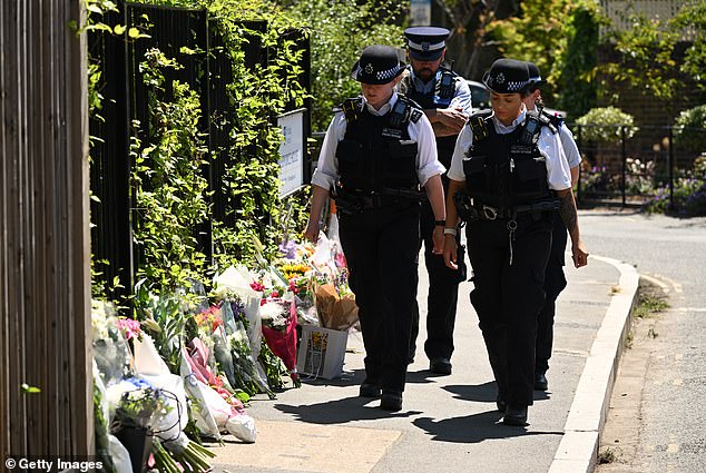 Police officers walk past flowers left by members of the community in tribute to the victims of a car crash outside The Study Preparatory School on Camp Road on July 7 last year