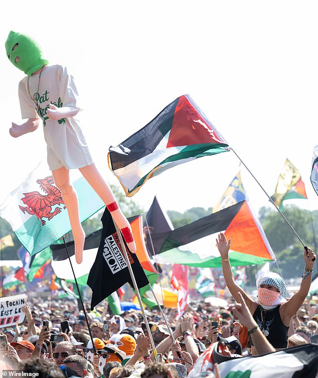 Crowds watching Kneecap hold up Palestinian flags and shirts for Palestine Action