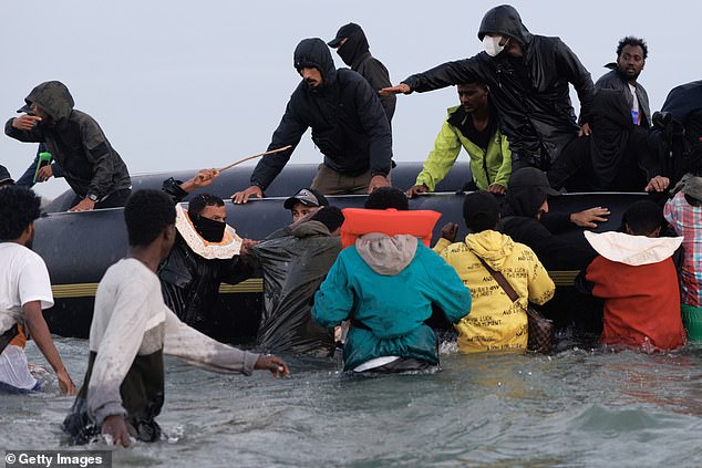 Traffickers, (with their faces covered) try to manage the scene using sticks as migrants wade into the water to be collected by a small boat at sunrise