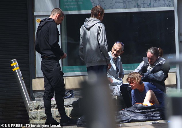 A woman sits in a sleeping bag on the pavement in an area nicknamed Crack Alley by locals