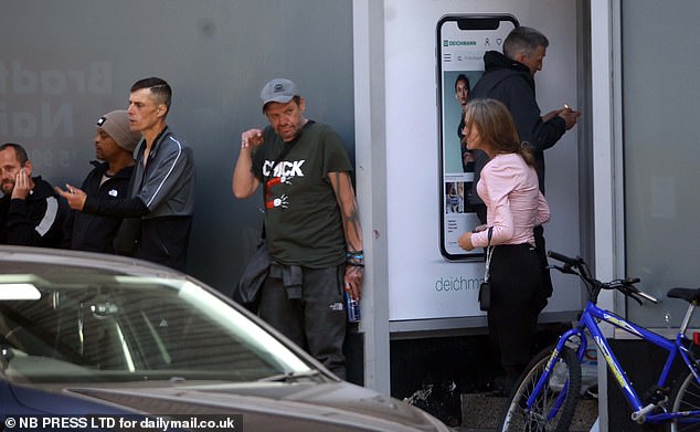 A man makes a strange gesture with his hand as another man huddles over a pipe in a doorway
