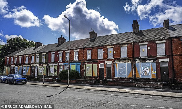 A row of houses that have been boarded up, with graffiti across it reading 'NOWHERE'
