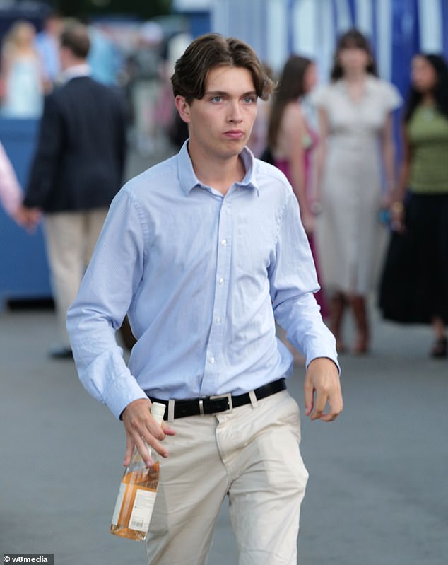 One male wearing an egg shell blue shirt and beige trousers holds onto a bottle of rose wine