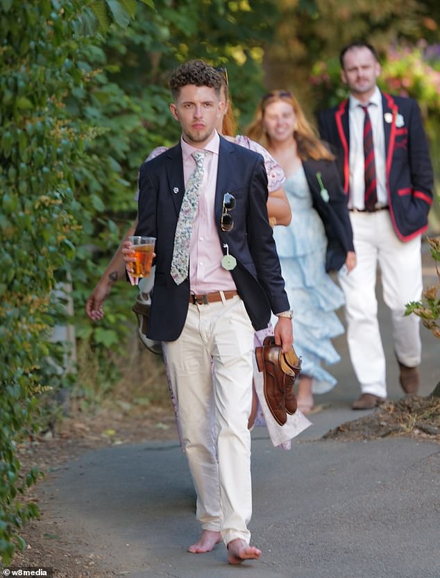A man carries his shows and walks barefooted on the ground at the Henley Regatta