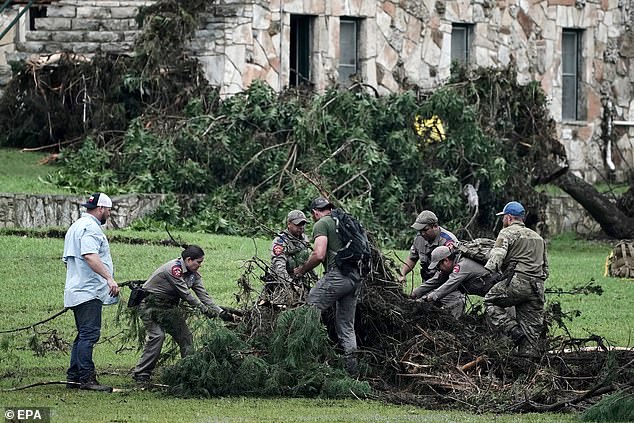 Emergency personnel search through vegetation and debris at Camp Mystic