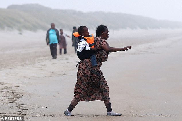 A woman and her child walks with a group of migrants on the beach to reach an inflatable dinghy in an attempt to cross the English Channel to reach Britain, at the beach of Petit-Fort-Philippe in Gravelines, near Calais, France, July 2, 2025