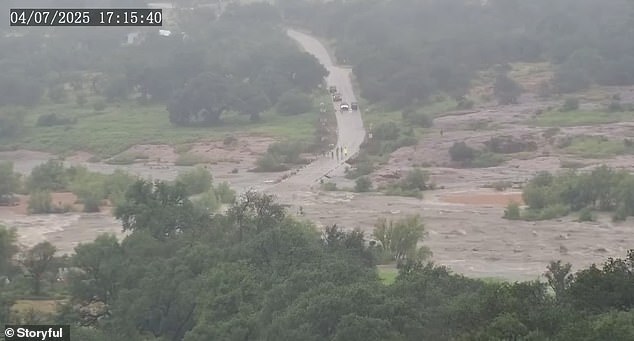 From around 5:15pm to 5:20pm the murky waters can be seen sweeping over a road while completely engulfing the smaller trees and bushes its path