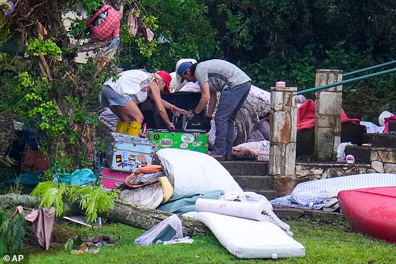 People look through belongings on a camp trunk at Camp Mystic along the banks of the Guadalupe River after a flash flood swept through the area Sunday, July 6, 2025, in Hunt, Texas. (AP Photo/Julio Cortez)