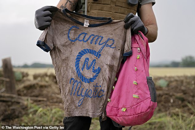 A search and rescue volunteer holds a T-shirt and backpack with the words Camp Mystic on them