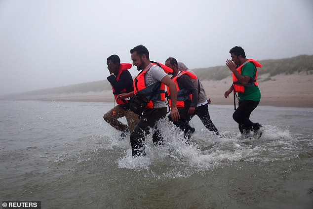 A group of migrants walk through the water to reach an inflatable dinghy in an attempt to cross the English Channel to reach Britain