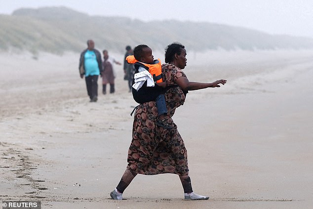A woman and her child walks with a group of migrants on the beach to reach an inflatable dinghy in an attempt to cross the English Channel to reach Britain