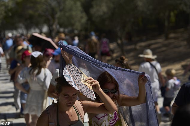 Tourists take cover from the sun outside the entrance of the Acropolis hill during a heat wave in Athens, Wednesday, July 9, 2025