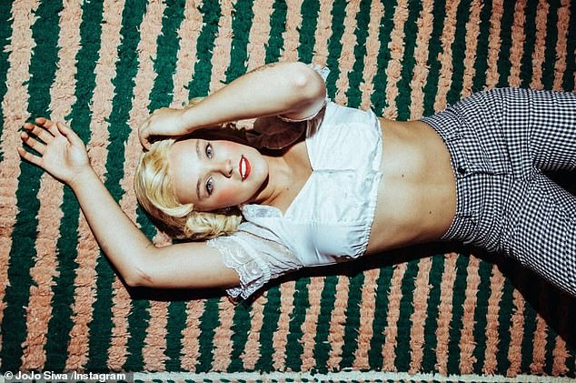 She displayed her taut midriff in a lacey crop top with frilly sleeves and a pair of black and white gingham trousers, while sporting a 1930s style curly blonde wig - but can you guess who it is?