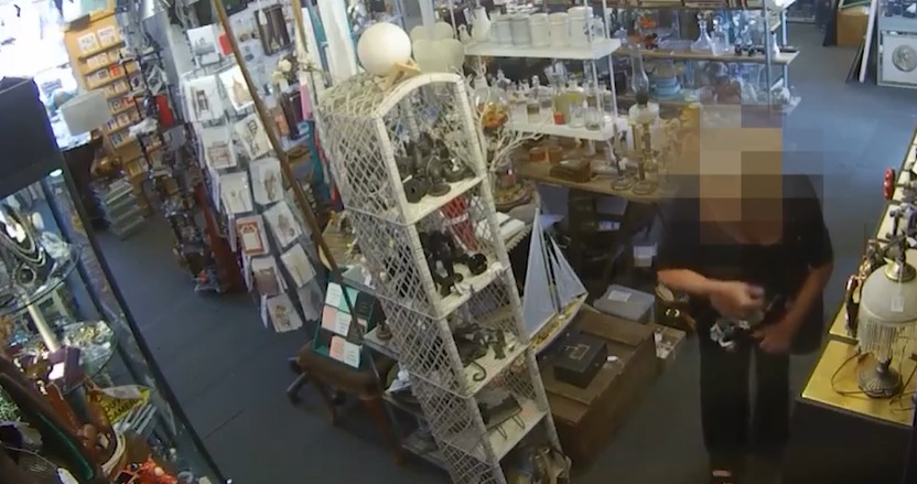 Security camera footage of a shop interior; a person is examining items on a shelf.