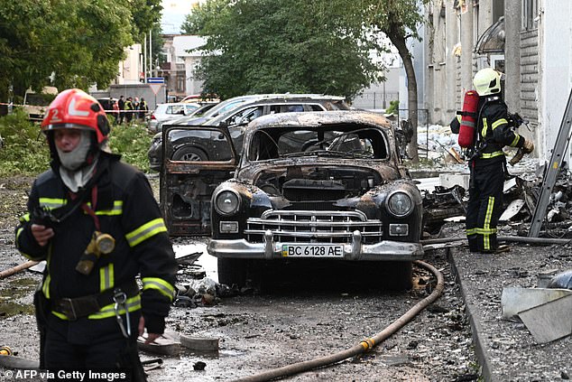 Two people were confirmed killed in Chernivtsi, close to the Romanian border, with at least 18 wounded in the overnight strikes which yet again targeted civilians. Pictured: Firefighters stand next to a burnt-out car following mass Russian drone and missile strikes in the western Ukrainian city of Lviv