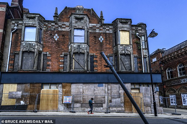 A grand architectural building left in disrepair. The store beneath is boarded up while the apartments upstairs can be seen degrading