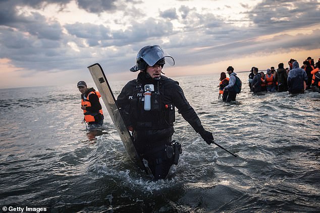 French Police enter the water to try and stop migrants boarding small boats that had come to collect them from further down the coastline on June 13, 2025 in Gravelines, France