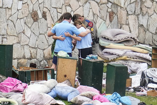 An officer prays with a family as they pick up items at Camp Mystic in Hunt, Texas on Wednesday, July 9