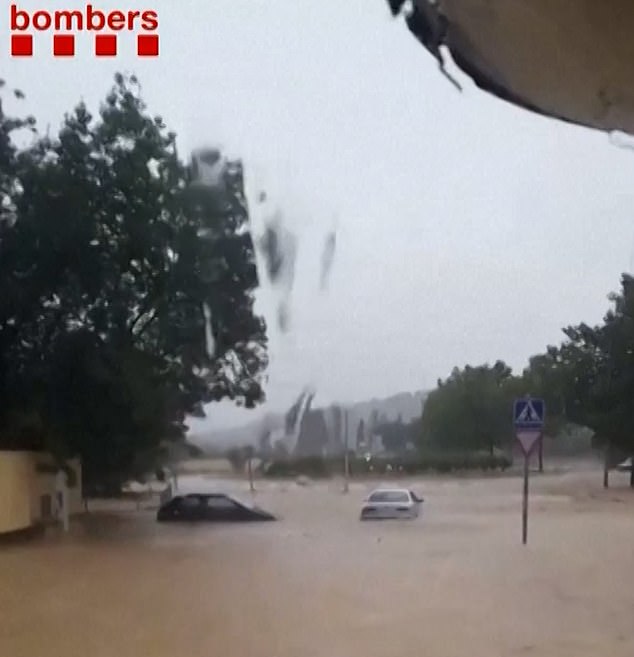 Cars are seen being swept away along flooded roads in Spain while other vehicles are completely submerged in thick mud and debris