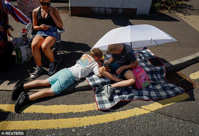 BELFAST: Children use smartphones under an umbrella that shields them from the sun on July 12, 2025