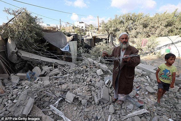 A Palestinian man and a child stand amid the rubble of a house in the aftermath of an overnight Israeli strike