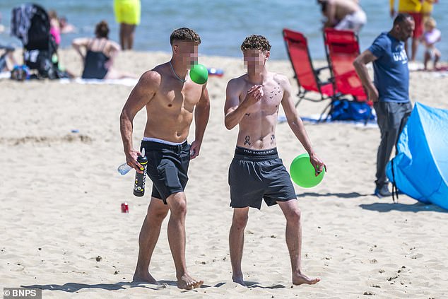 Two young revellers are seen walking along Bournemouth beach, one with a balloon in his mouth