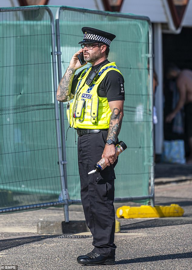 A police officer speaks on the phone while holding a canister of nitrous oxide on Bournemouth beach