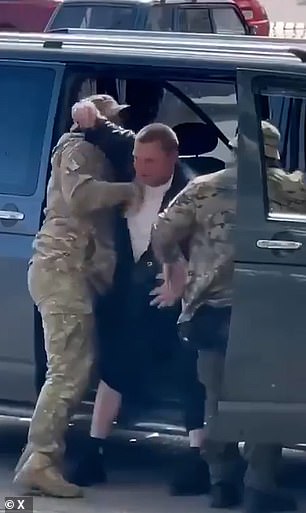 A Ukrainian men is pictured above as he is dragged into a vehicle by military recruitment officers