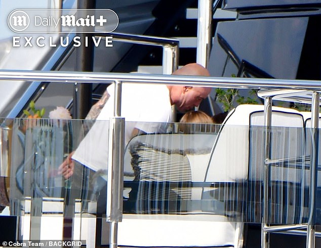 Rogan leans over to talk to his family as they recline on white leather seats on the bridge deck