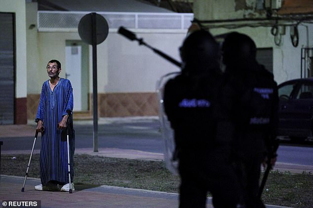 A man on crutches stands near riot cops during their patrols of the town