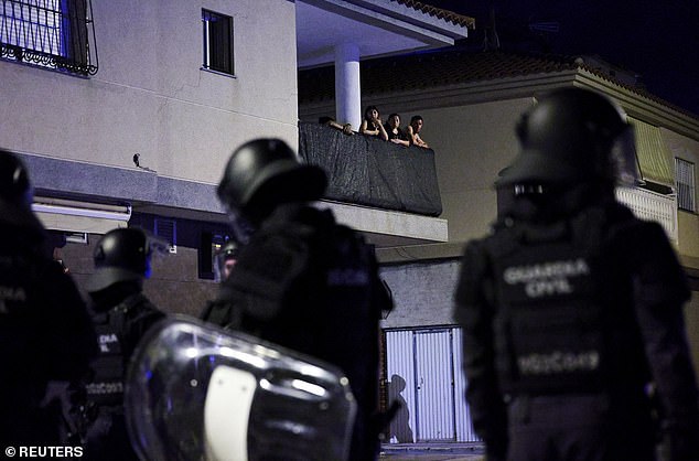 People watch from a balcony as police officers keep watch amid anti-migrant unrest in the Murcia town
