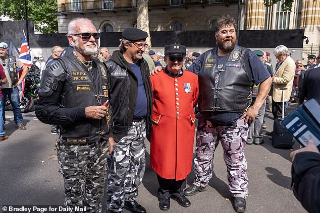 Three veterans in leather biker jackets and combat pants pose next to a Chelsea pensioner in signature red jacket at the protest
