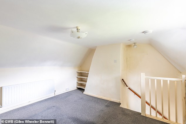 An upstairs room with cream walls, a large chimney breast and stairs straight down to the ground floor