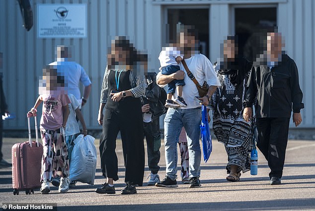The migrants, including babes in arms, head for their bus at Stansted