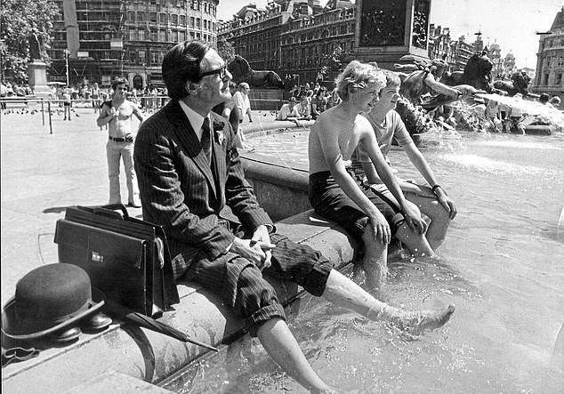 A businessman sits with his trousers rolled up and his legs planted in the water of the fountain at Trafalgar Square