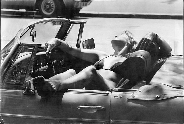 A woman in a Bikini lies sideways in her convertible sports car during the summer of 1976