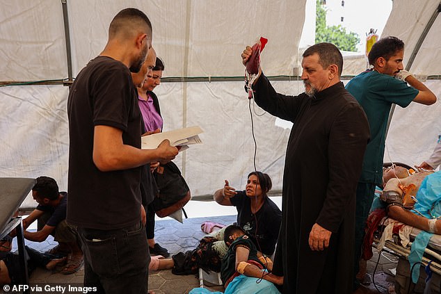 Father Carlos (C) from the Holy Family church in Gaza City assists casualties injured in an Israeli strike