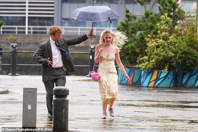 A man tries to keep a woman dry while walking in the rain at Newcastle Quayside on Tuesday