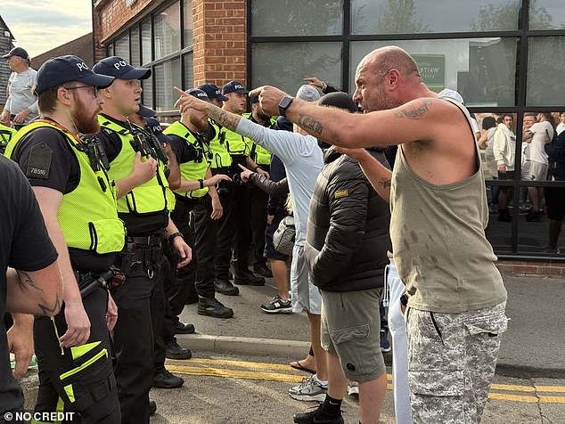 A line of men shout at police as they form a human baricade between the protestors and the anti-racism counter-protesters