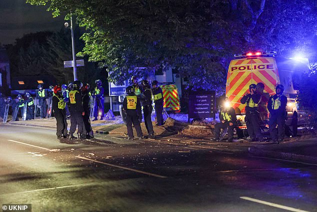 Police officers stand in a street covered in smashed glass and other debris