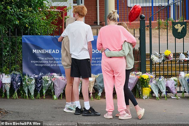 People comfort each other as they look at the floral tributes at the entrance to the Minehead Middle School in Minehead Somerset