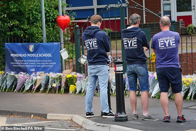 People look at the floral tributes at the entrance to the Minehead Middle School