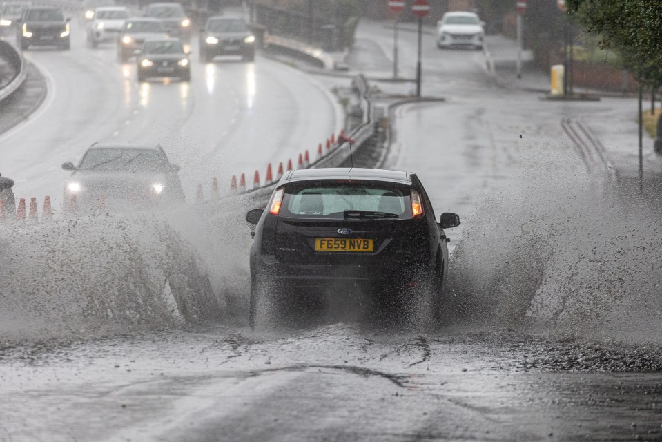 Car splashing through deep water on a flooded road.
