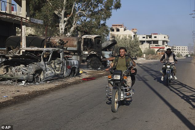 Bedouin fighters ride motorcycles past burned vehicles in Mazraa village on the outskirts of Suwayda city