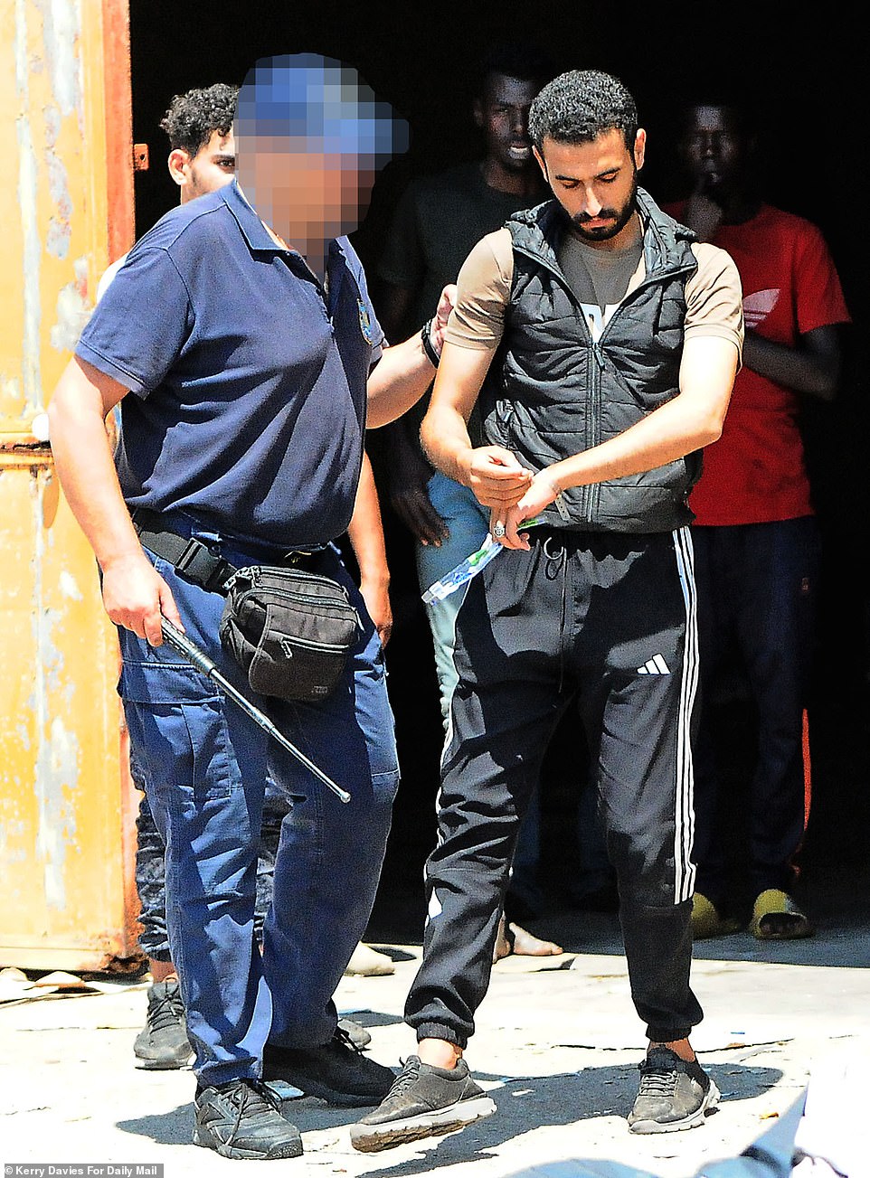 A coast guard office holding a stick is seen handling a migrant after a row at the the camp which threatened to run out of control