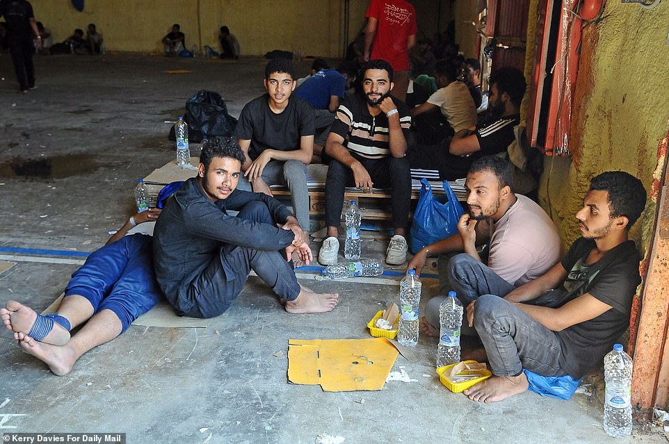 Migrants are seen sitting on the floor of the Kitrenosi facility with water bottles to stay hydrated