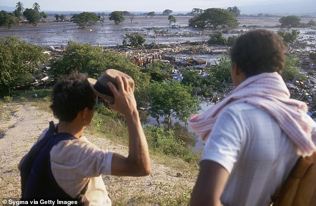Two men look out over a field of mud, where a lahar from the erupting Nevado del Ruiz volcano flowed into a valley in Colombia