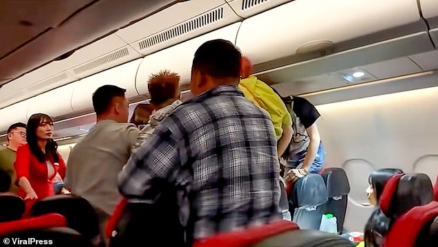 Desperate cabin crew members and other passengers can be seen wrestling with those involved in the scuffle