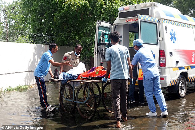 Pictured: A policeman and medics transferring bodies of victims onto an ambulance after the Air India Flight 171 crash