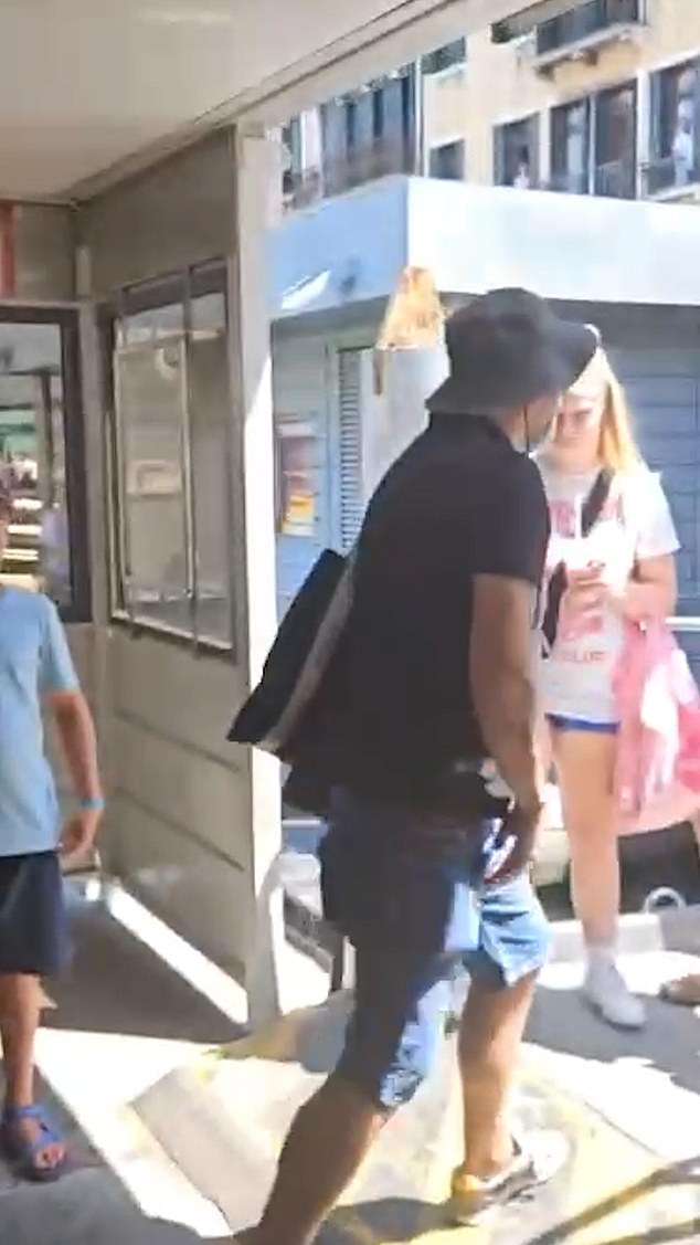 A man dressed in a yellow T shirt, bucket hat and carrying a rucksack and as he spots that he is being filmed he darts off into the street